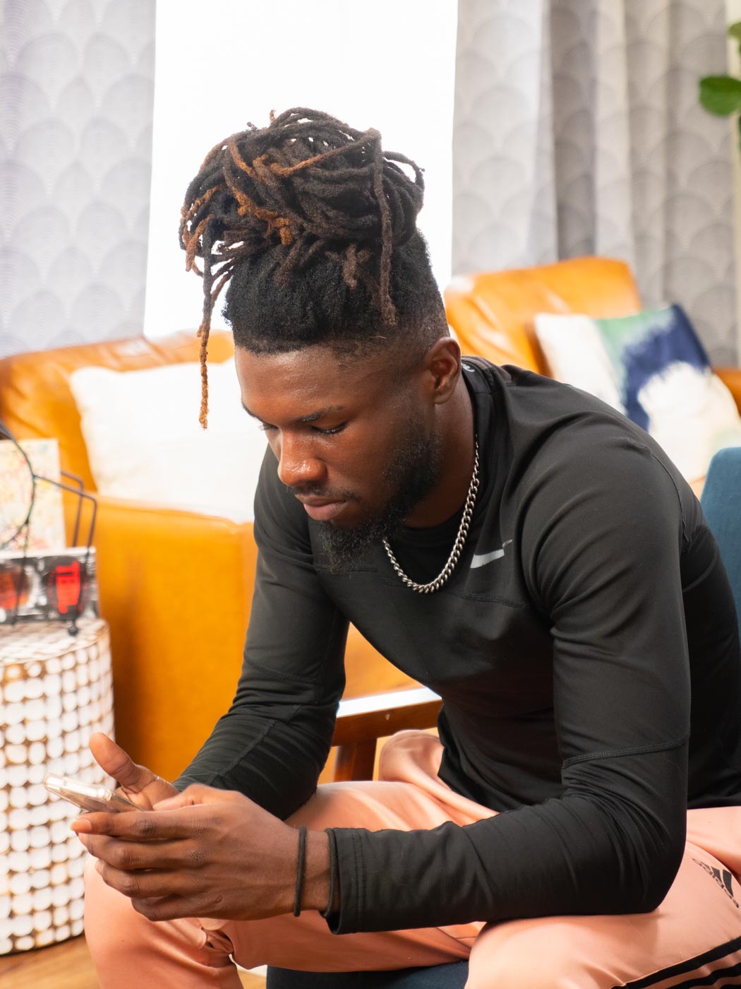 A photograph of an African American, male-presenting youth looking at their smartphone sitting in a living room.